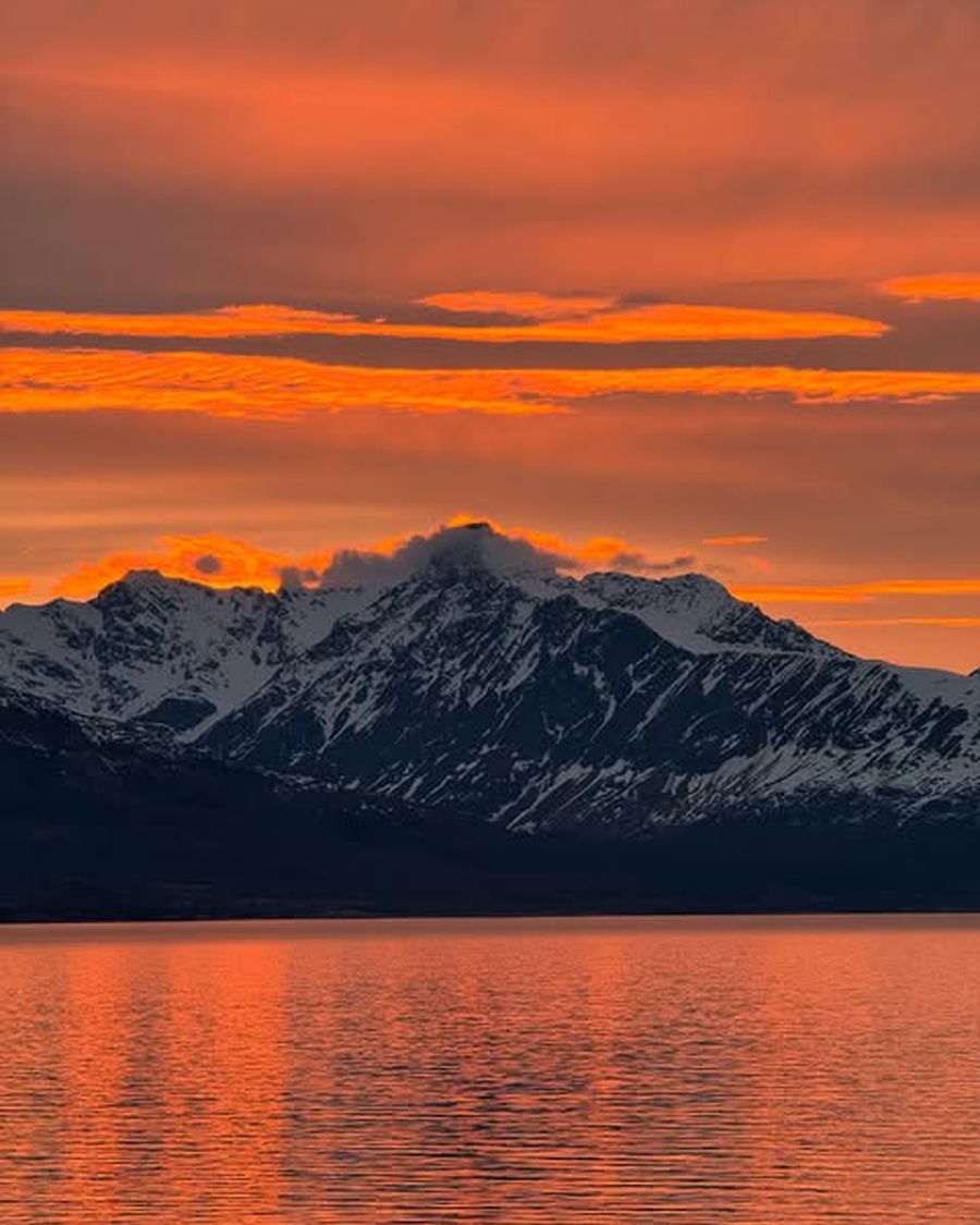 Oransje kveldshimmel over snødekte fjell og stille vann.