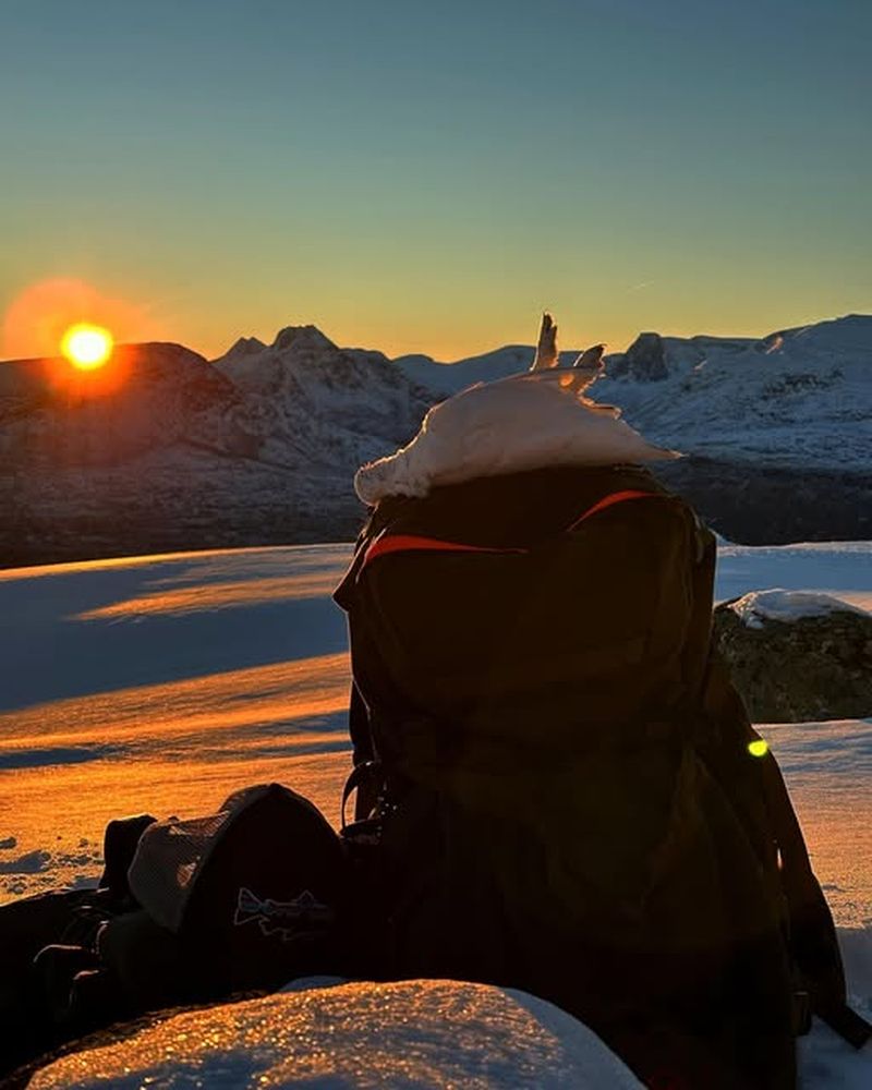 Jaktsekk i solnedgang med rype på lokket, fjell i bakgrunnen.